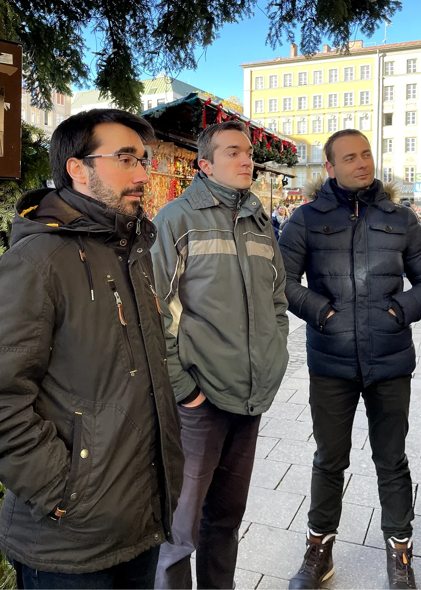 Martin steht mit zwei Kollegen auf einem Weihnachtsmarkt, alle warm eingepackt und im Gespräch: winterlicher Team-Moment in entspannter Atmosphäre.